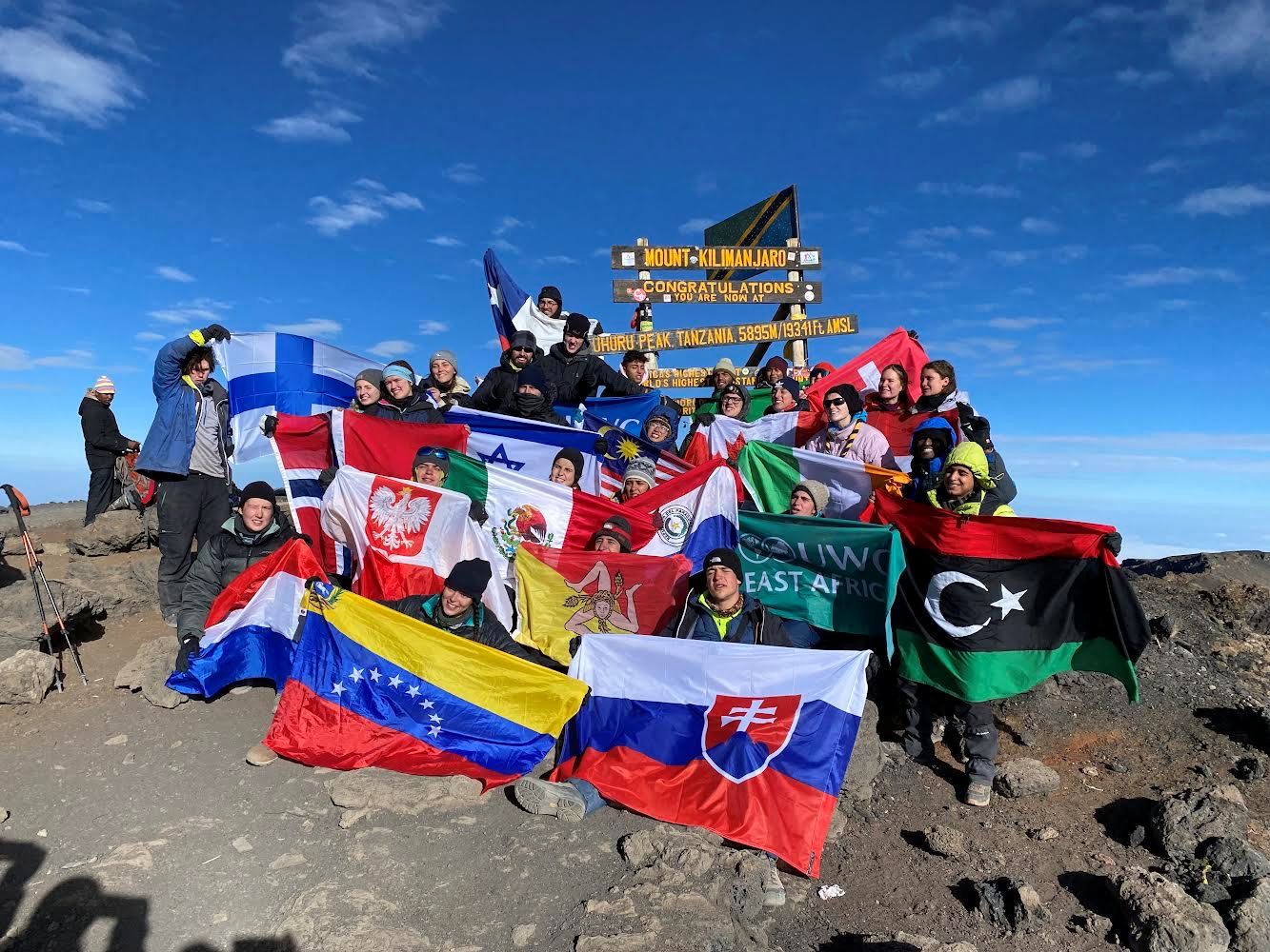 Students summit mountain and wave their national flags